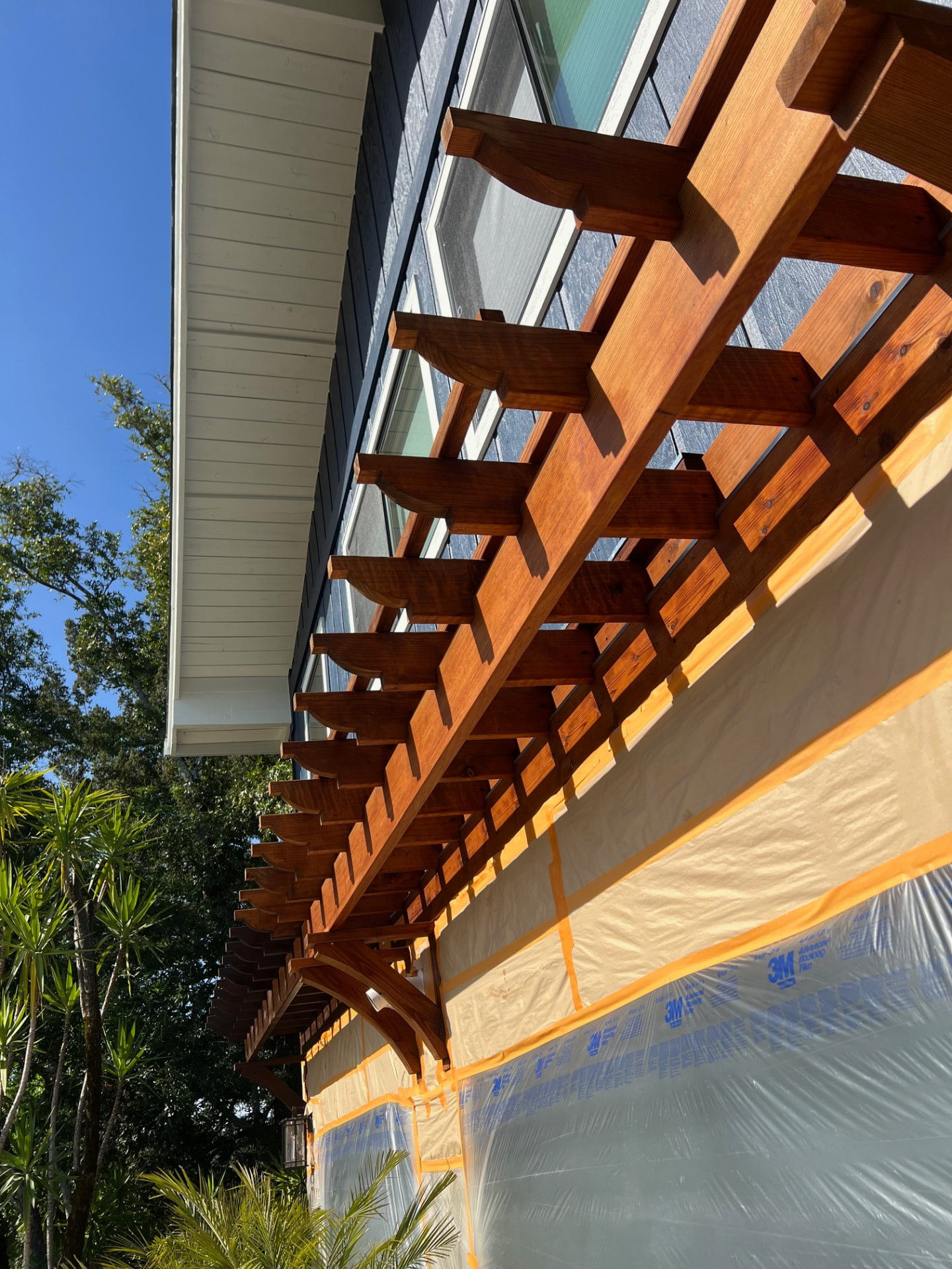 Freshly stained redwood pergola against repainted siding